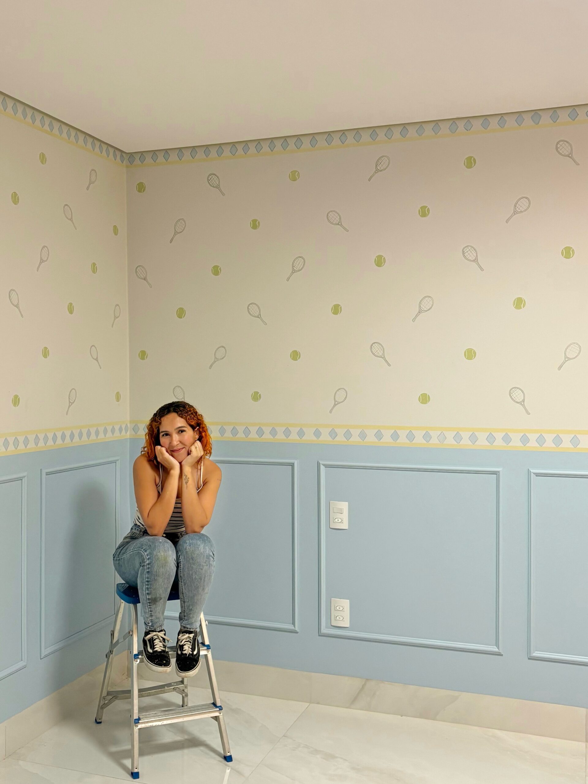 Jessica sentada em um ambiente com mural delicado e meia parede azul