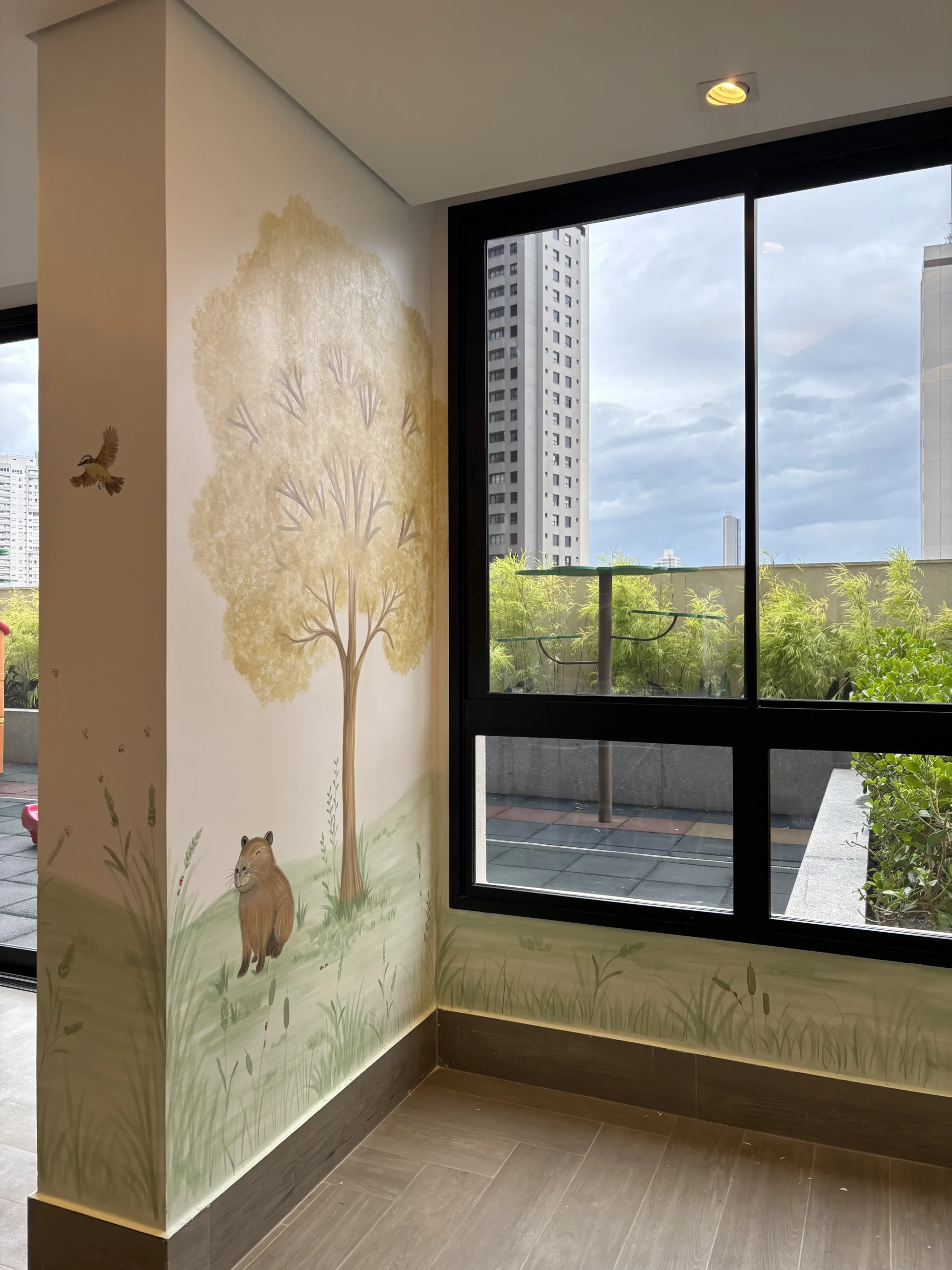 Mural de árvore e animais ao lado de uma janela ampla