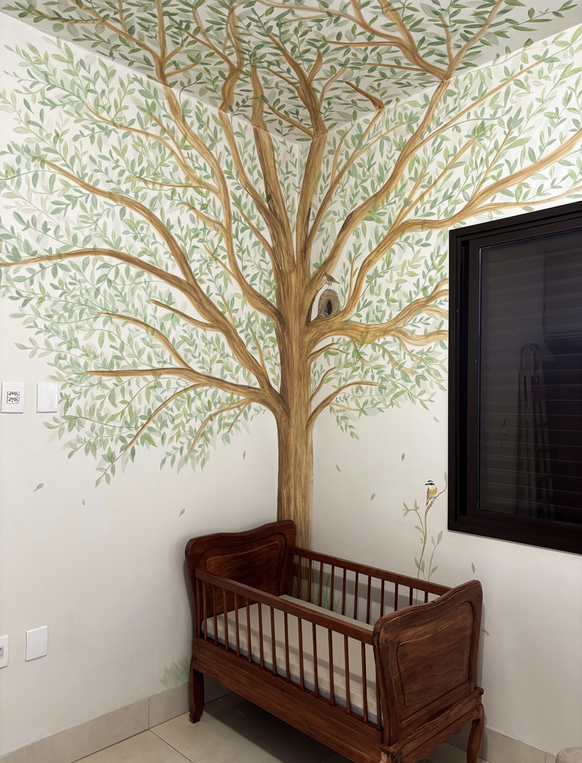 Árvore pintada à mão envolvendo o berço de madeira em um quarto de bebê