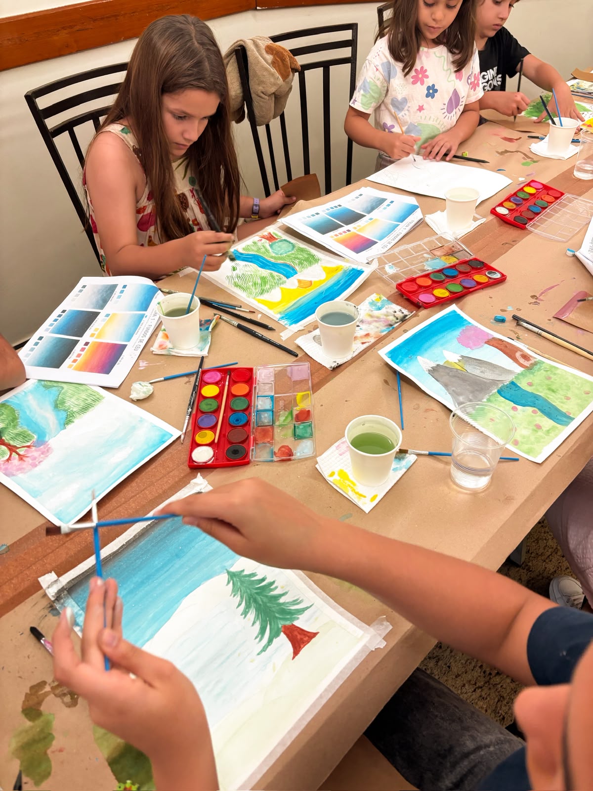 Crianças pintando paisagens em aquarela, cada uma com seu próprio desenho
