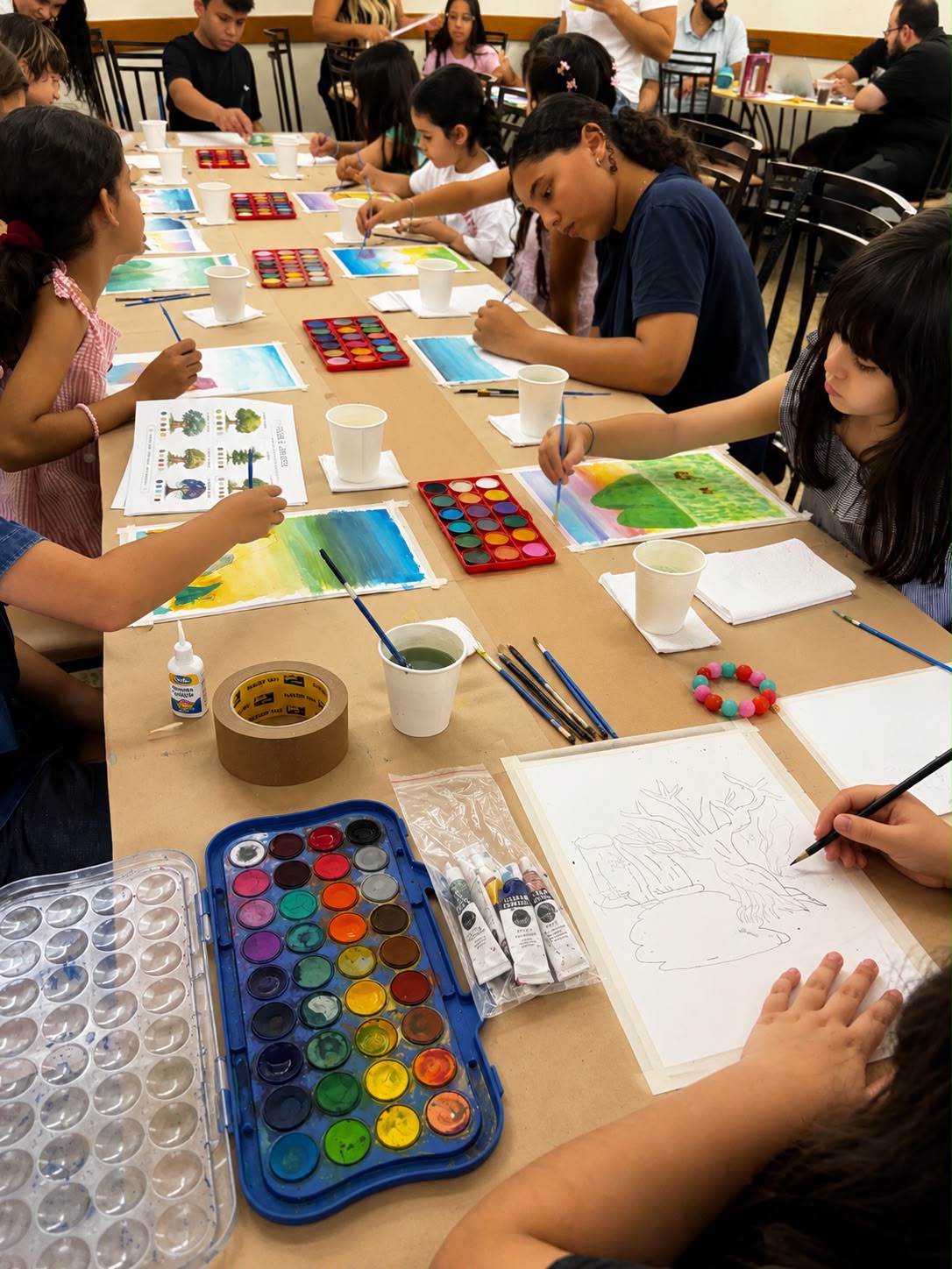 Grupo de crianças pintando aquarelas lado a lado em uma mesa longa